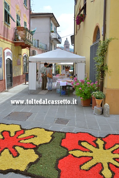 BRUGNATO (Infiorata del Corpus Domini 2014) - Il tappeto floreale scorre in Via Roma. Fanno da sfondo i gazebo del mercatino agroalimentare e il campanile della chiesa