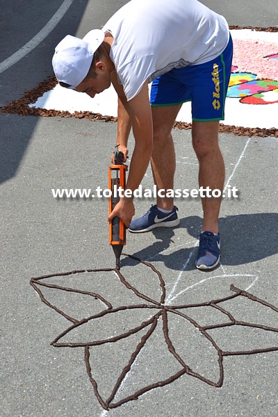 BRUGNATO (Infiorata del Corpus Domini 2017) - Un infioratore utilizza una pistola per silicone opportunamente modificata per disegnare con fondi di caff i contorni di un disegno geometrico