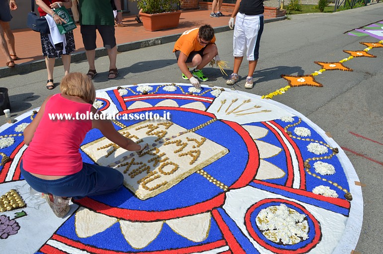 BRUGNATO (Infiorata del Corpus Domini 2014) - Disegno circolare con testo "Ama Deum, Ama Proximum", realizzato con sale, sabbia colorata, fondi di caff, frutti secchi e fiori freschi