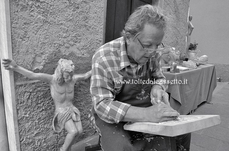 SAN PIETRO VARA in fiera - L'artista del legno Sergio Vettori al lavoro su un bassorilievo. Dietro di lui la scultura del Cristo in croce