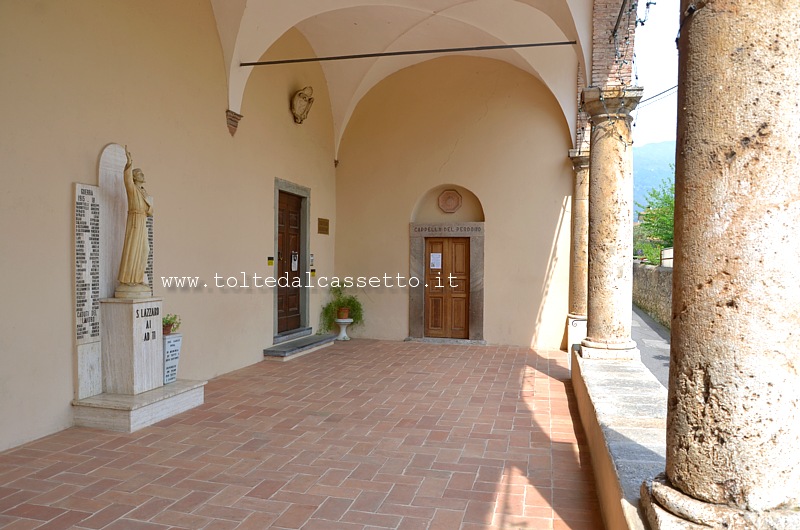 CAMAIORE - Portico dell'Ospedale di San Lazzaro con monumento ai caduti in guerra. Sullo sfondo la porta di entrata della "Cappella del Perdono"